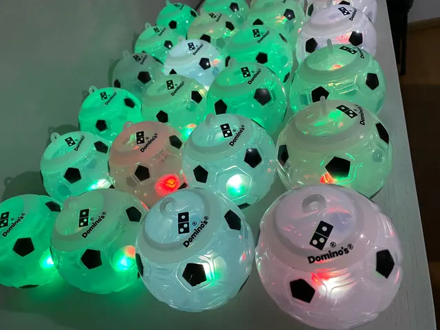 Balones de futbol luminosos y translúcidos con el logo de Domino's, encendidos en verde, blanco y rojo