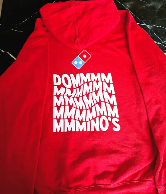 Espalda de una sudadera roja con el logo de Domino's y un estampado blanco de letras onduladas